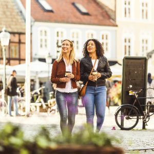 Two women with coffee cups walking on city street