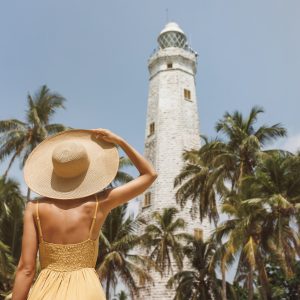 Woman traveler in dress and hat in front of famous landmark of Sri Lanka country, Dondra lighthouse