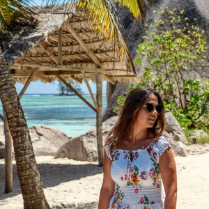 Young woman wearing sunglasses and floral dress standing on sandy beach
